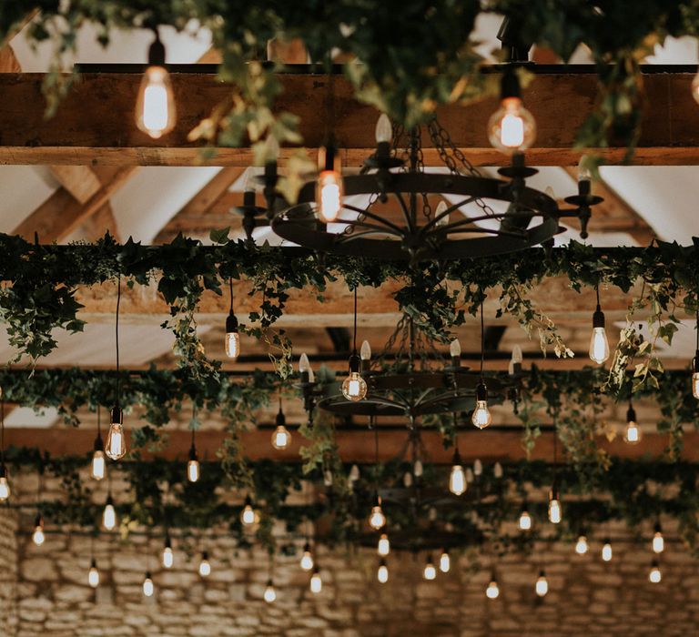 Hanging pendant lightbulbs and ivy foliage hanging from beams in stone barn wedding at Caswell House