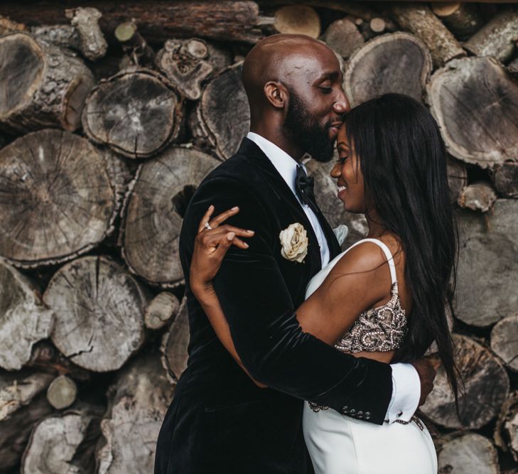 A bride and groom embrace. He kisses her on the forehead.