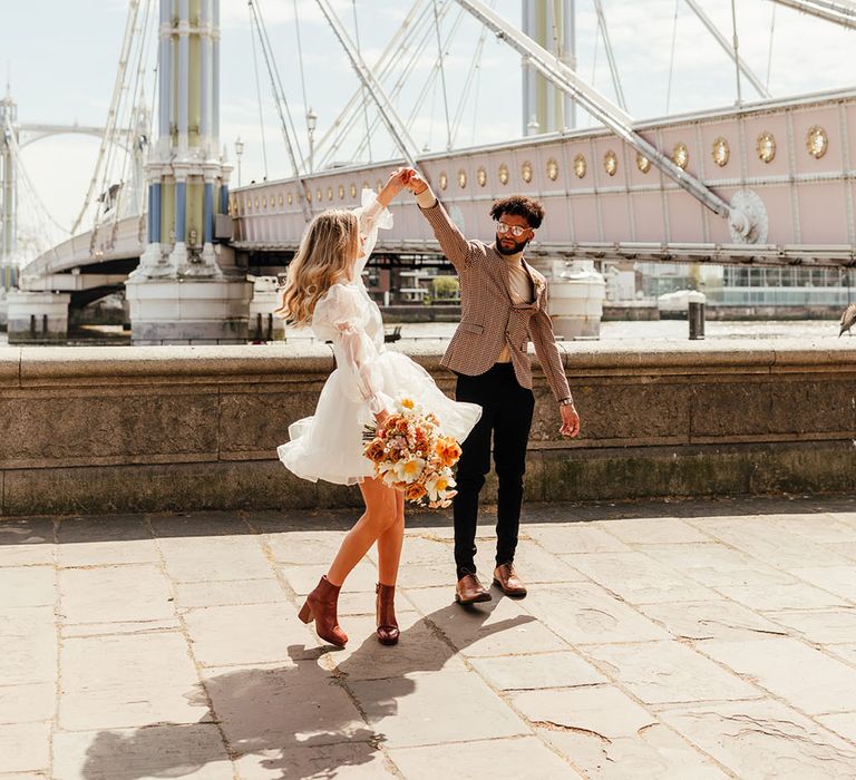 Stylish groom in a check blazer twirling his bride in a short ruffle wedding dress and boots 