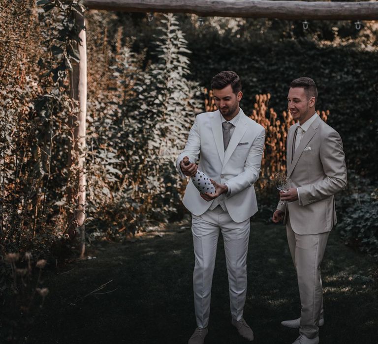 Grooms pop champagne in light grey wedding suit