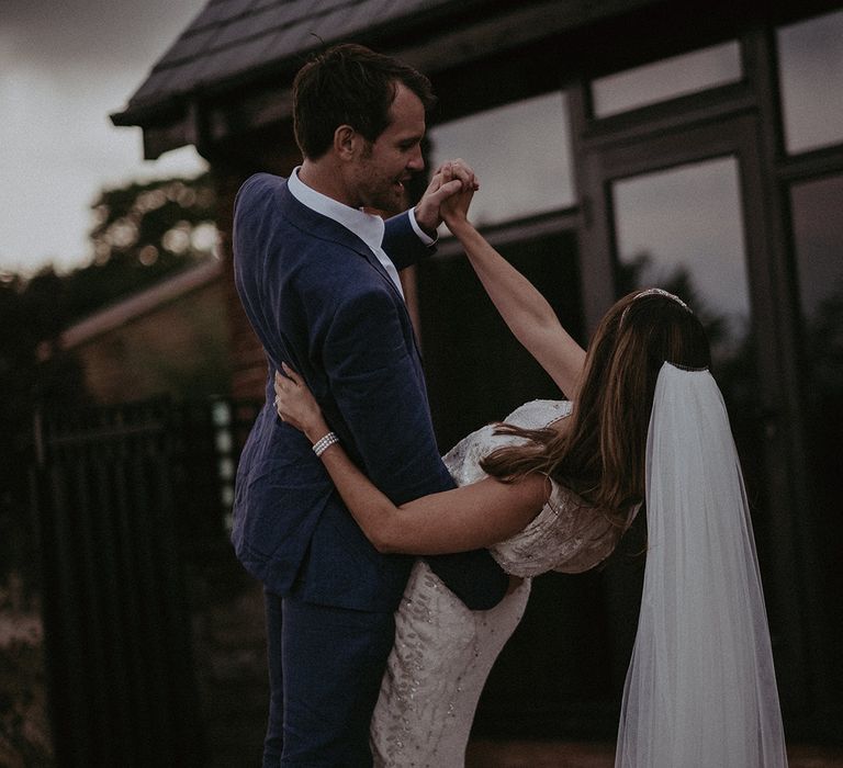 Groom dips bride as they dance outdoors during their wedding reception