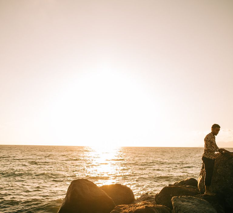 Groom helps bride on to the rock to watch the sunrise in Santorini 