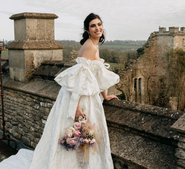 Bride wears large white wedding gown with puffed sleeves and holding pastel bouquet