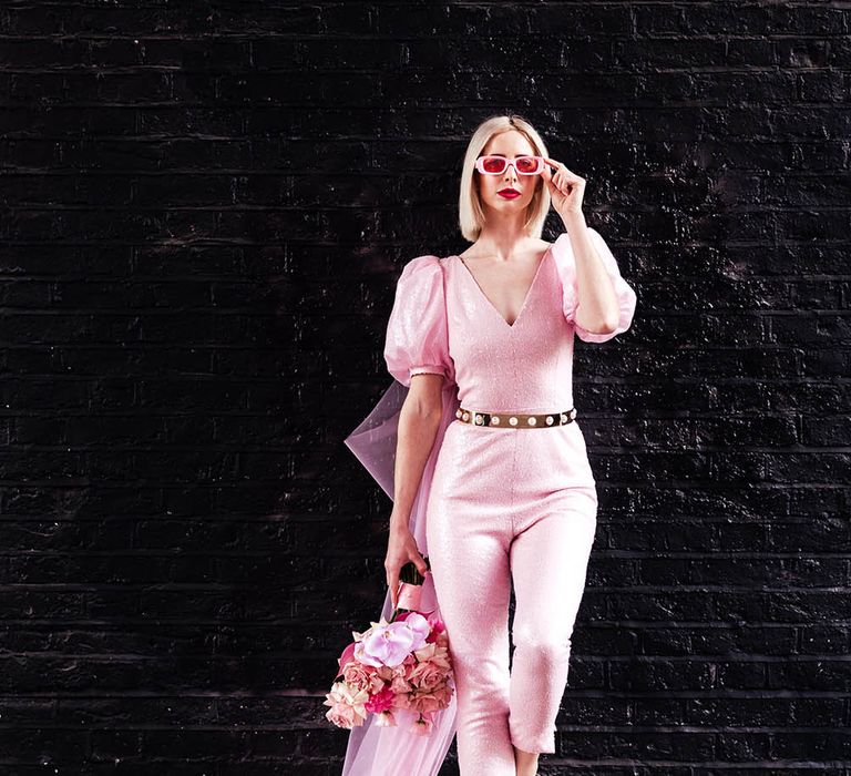 Bride in a fitted pink jumpsuit with gold belt and blush bouquet 