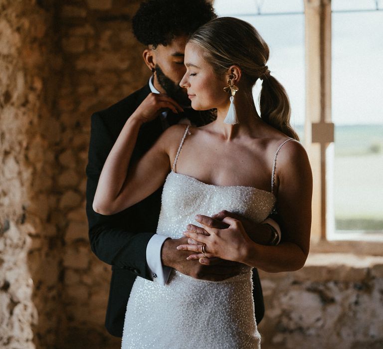 Groom in a black tuxedo embracing his bride in a sparkly wedding dress and tassel earrings 