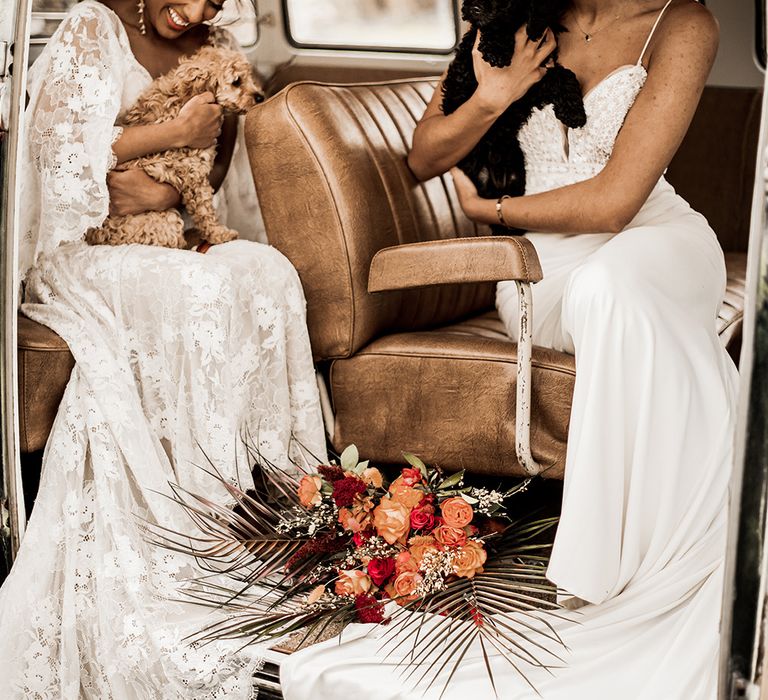 Two brides in a lace and fitted wedding dress holding a tan and black cockapoo puppy inside a VW camper van at their farm wedding venue 