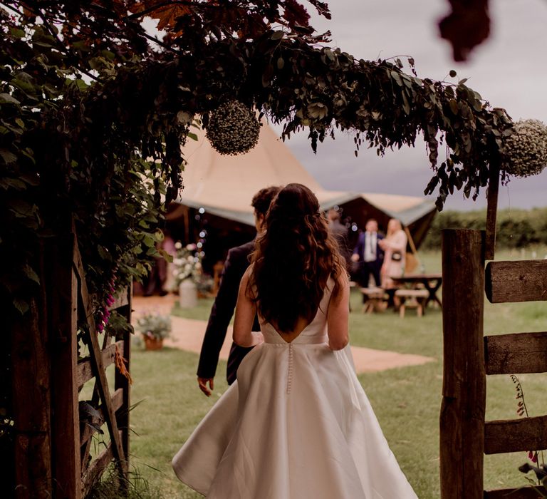 Bride in white low back Elbeth Gillis wedding dress with buttons walking towards tipi home farm wedding 