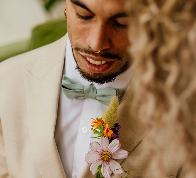 Groom in beige suit with green floral bow tie and wildflower buttonhole flower 