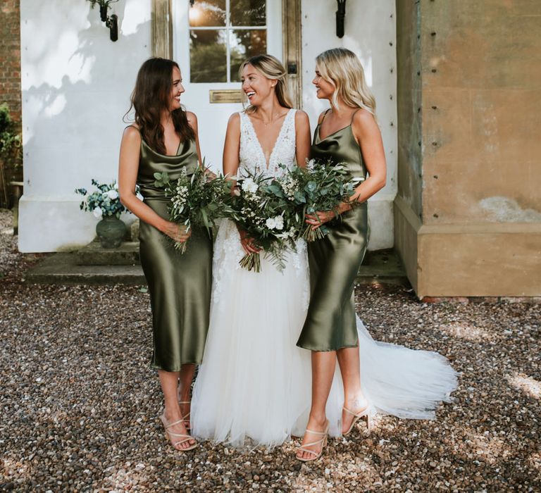 Bridal party portrait with bridesmaids in green satin slip midi dresses holding foliage bouquets