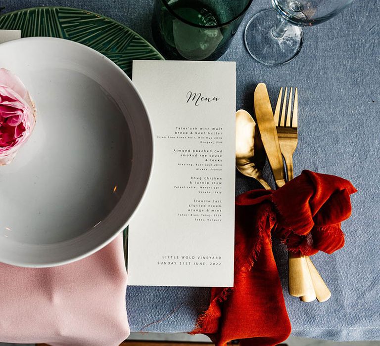 Place setting with coloured tableware, gold cutlery and menu card 