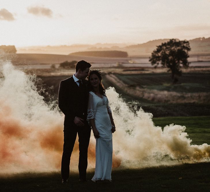 Bride and groom portrait in a field with an orange smoke flare blowing across the ground 