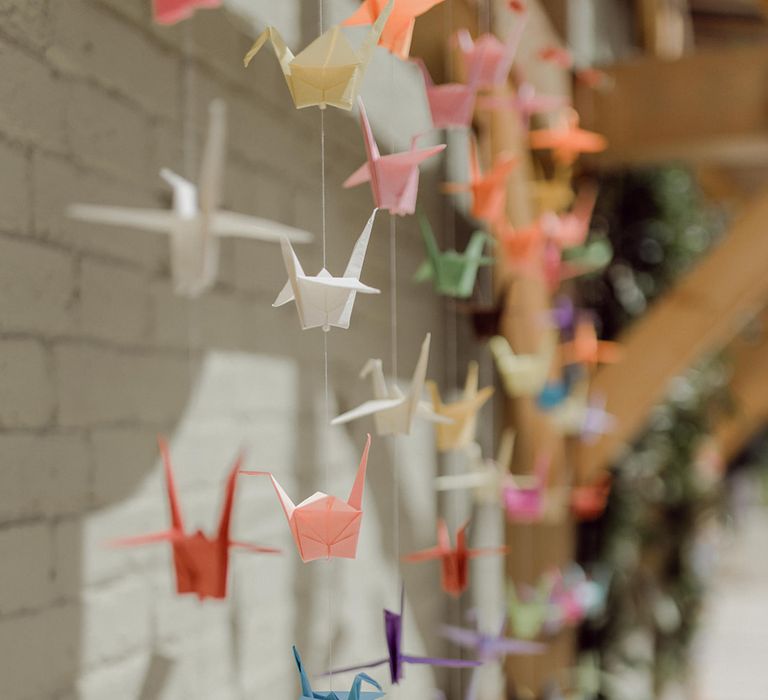 Handmade colourful paper cranes hanging from wall  | Joshua Gooding Photography