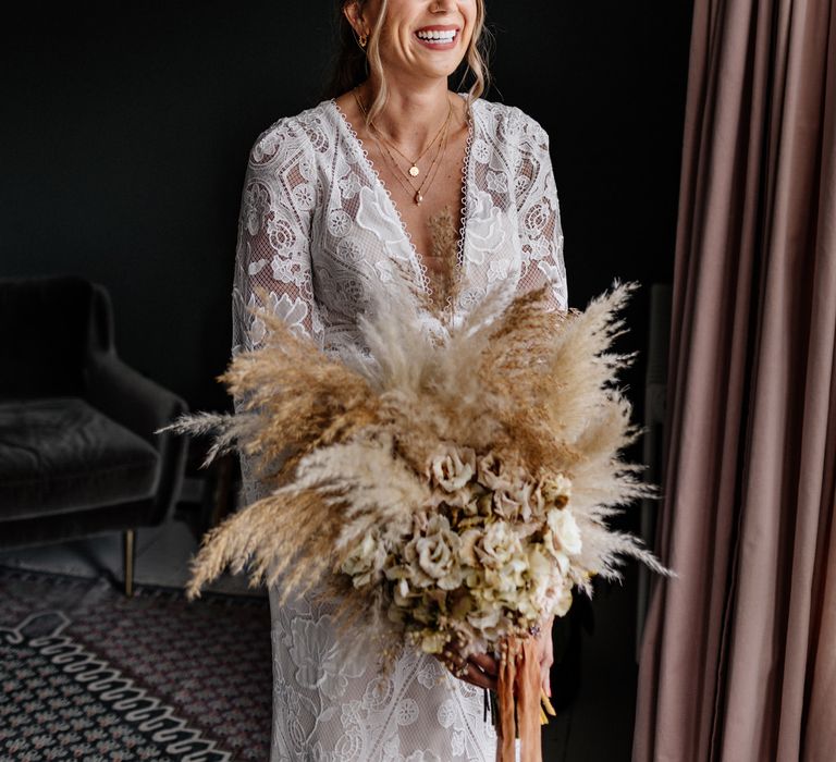 Bride in boho dress clutches neutral bouquet with pampas grass