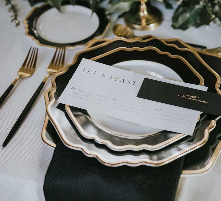 Sophisticated place setting with black and white plates with gold rim and black and gold cutlery 