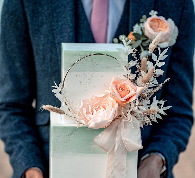 Groom holding a square two tier buttercream wedding cake with white and mint green ombre design 