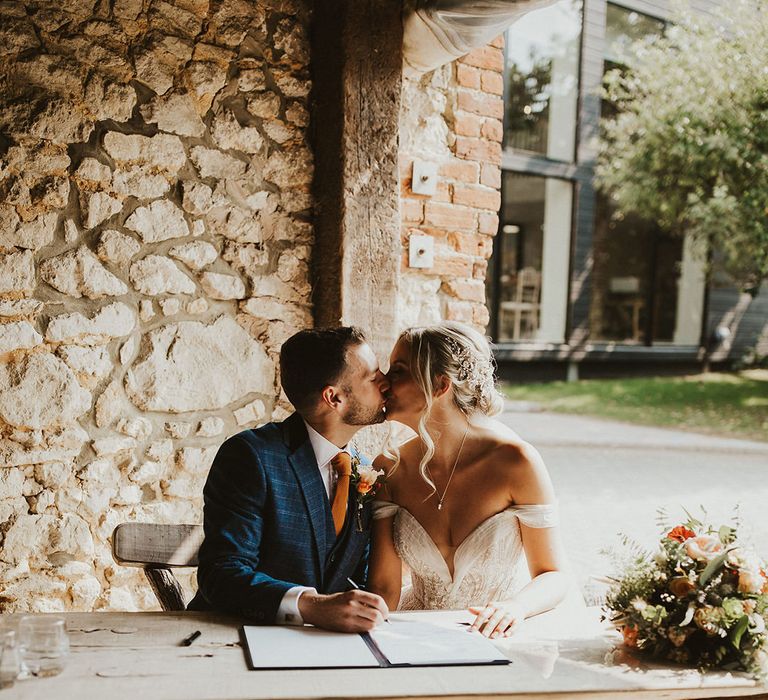 Bride and groom kiss as they sign a register