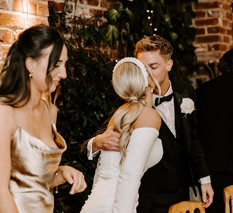 Bride in a strapless wedding dress with detachable long sleeves kissing her groom during the wedding reception speeches 