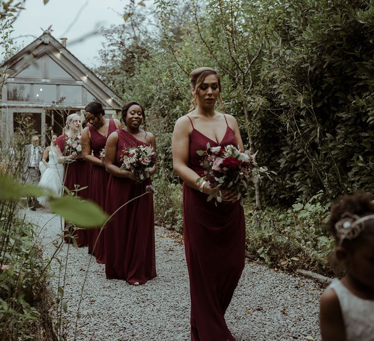 Bridesmaids walk to the aisle wearing burgundy dresses 