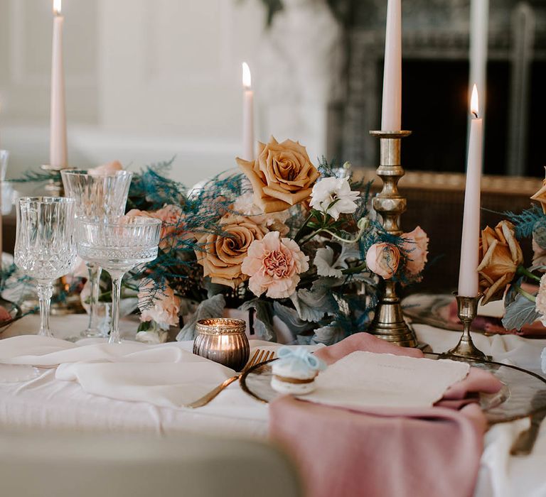 Elegant place setting with glass charger plate, pink linen, macaroon favour, gold candlesticks and blue wedding flowers 