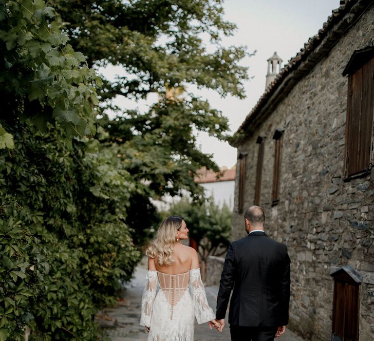 Bride & groom walk hand in hand through cobbled streets of Greece on their wedding day