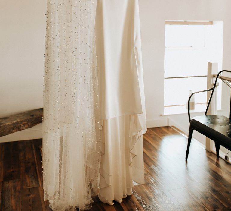 White cami wedding dress with mesh overlay encrusted with pearls hanging from beam