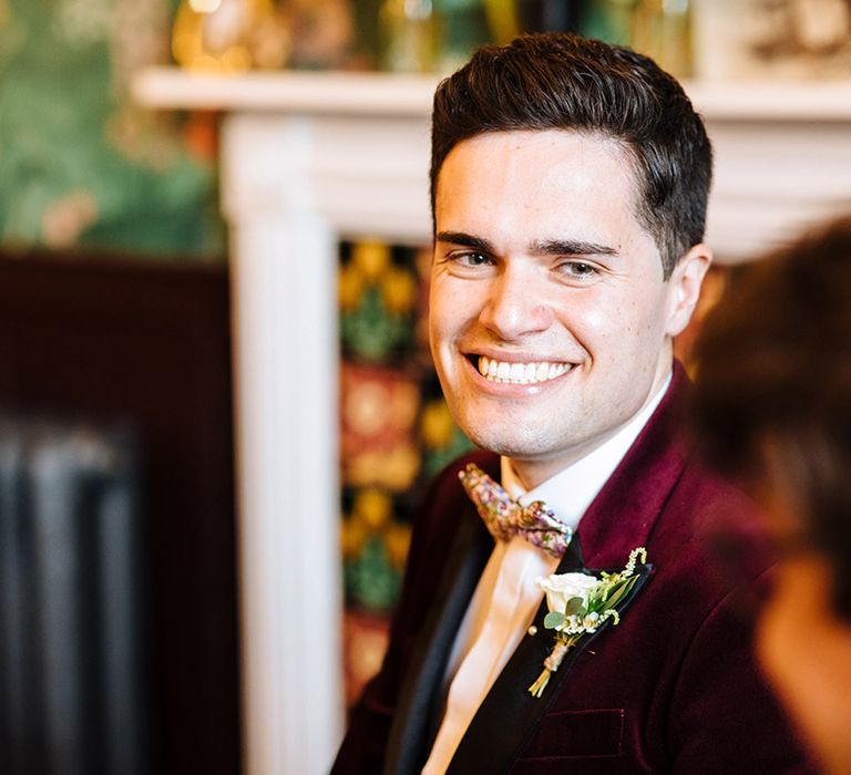 Smiling groom in burgundy velvet tuxedo jacket with white rose boutonnière