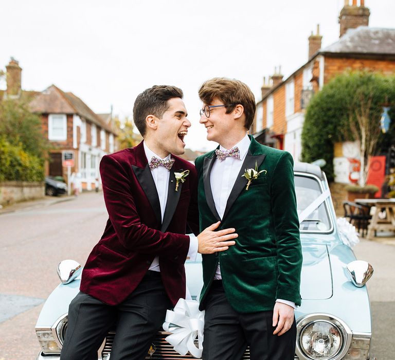 Grooms seated on vintage baby blue wedding car with velvet suit jacket