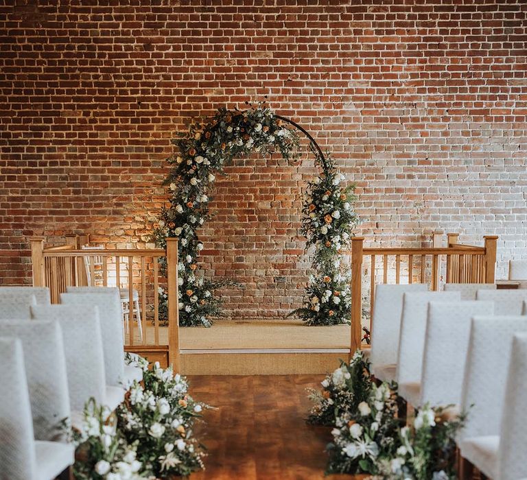 Aisle and altar style with white high back chairs and white and orange flowers with flower archway