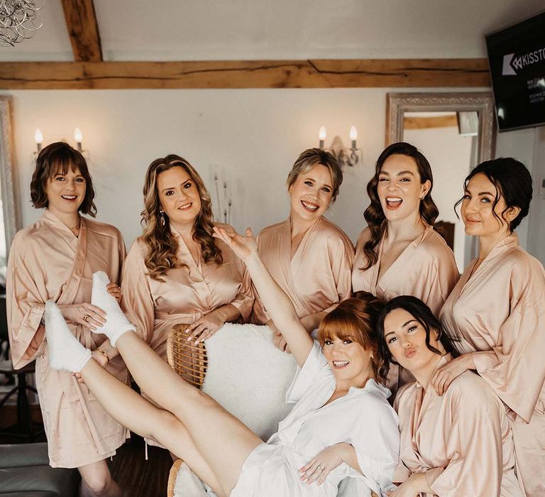 Bride in white dressing gown poses with her bridesmaids in pink dressing gowns with hair and makeup completed