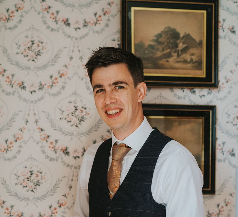 Ring bearer in checkered blue waistcoat and yellow tie holding wooden jewellery box contatining the wedding bands