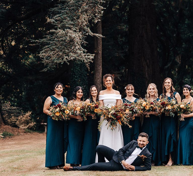 Bride in off the shoulder wedding dress with bridesmaids in blue dresses and groom in blue tie with autumnal wedding bouquets