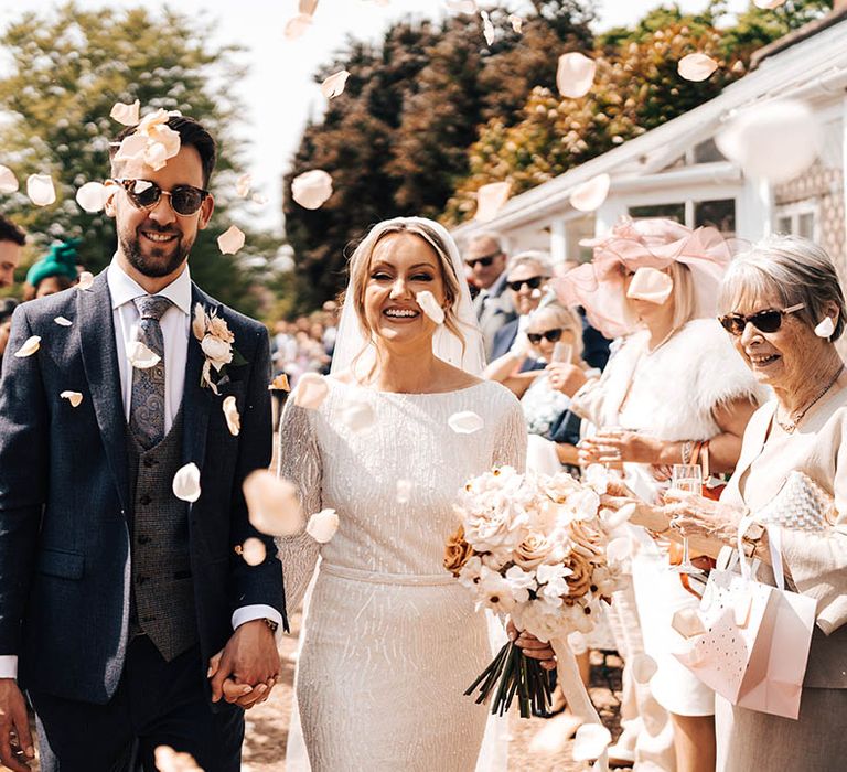 Bride and groom in sunglasses walk through pink rose petal confetti 