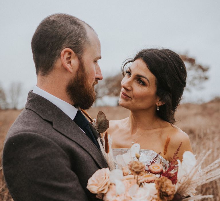 Bride and groom look deeply into each other's eyes with neutral wedding bouquet 