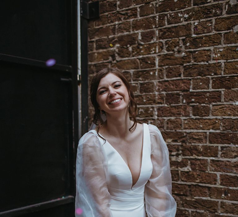 Bride smiles in Suzanne Neville wedding dress with custom sheer puff sleeves holding spring wedding bouquet with giant poppy