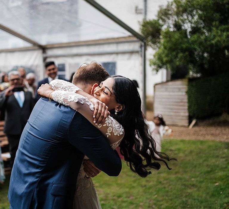 Bride and groom share an intimate embrace as their wedding guests stand and applaud for them