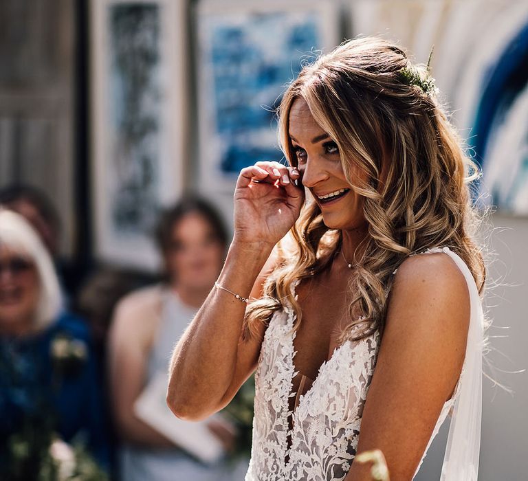 Bride in lace v-neck wedding dress with tulle wings wipes her eyes during ceremony 