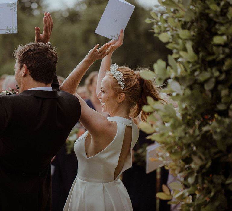 Bride and groom raise their hands in celebration as they sing 