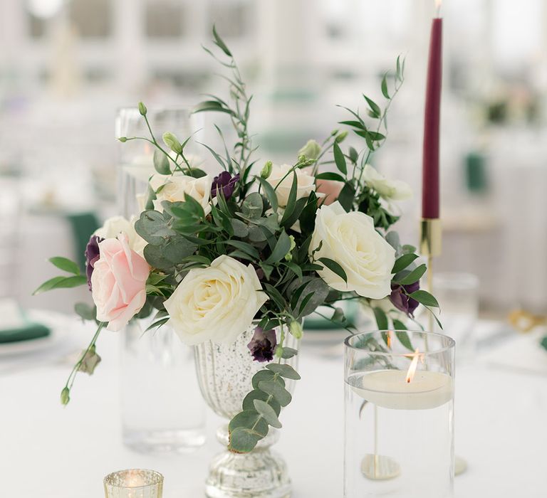 White & pale pink roses sit in vase beside candles placed on white tablecloths 