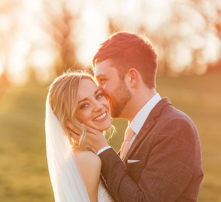 Groom smile as the bride turns her head to the camera as the sun sets 