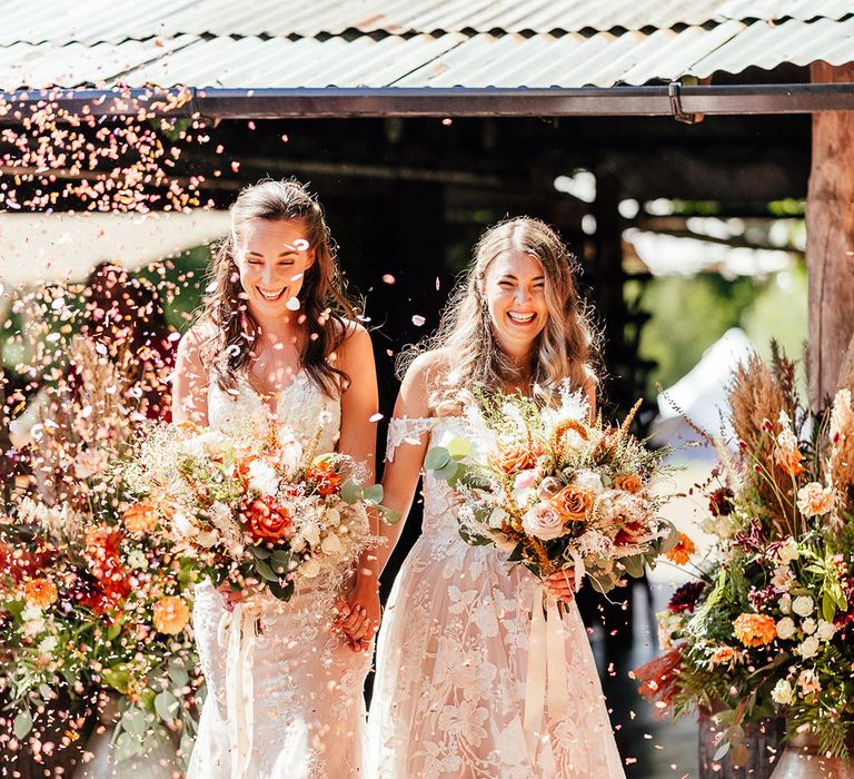 Brides laughing together as they walk out to confetti 