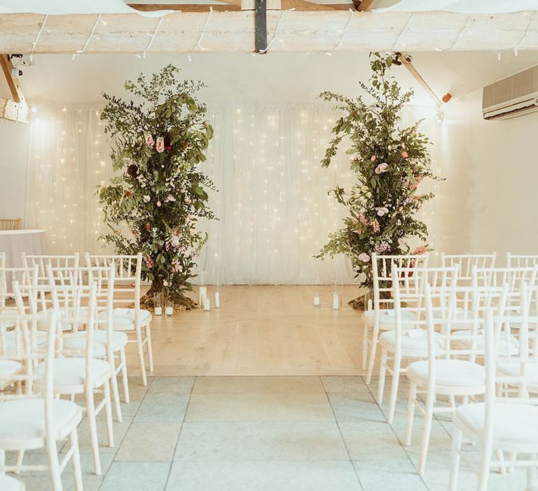 Two large wedding flower columns with pillar candles and hurricane vases with white chairs for the wedding ceremony 