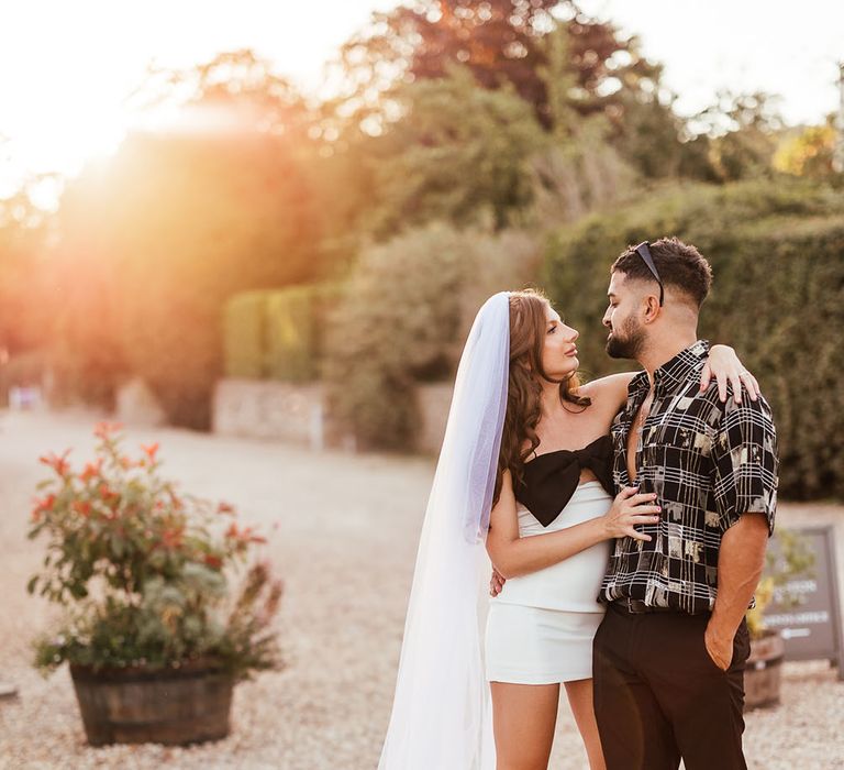 Bride wearing short wedding dress and black strappy heels looks at her who groom during golden hour portraits outdoors 