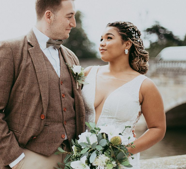 Groom in a brown checkered wedding suit standing with bride in a plunging neckline wedding dress with a white rose bouquet 