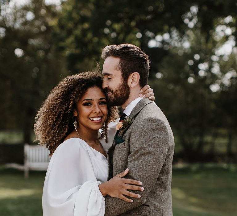 Black bride with a satin balloon sleeve wedding dress hugging the groom in a grey tweed suit 