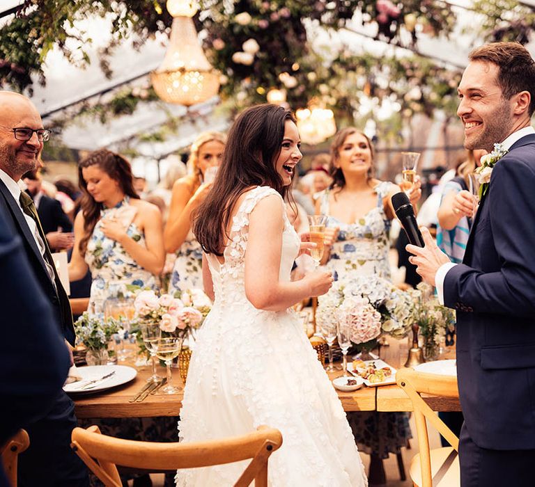 Wedding guests stand up as the groom delivers his wedding speech holding a microphone 