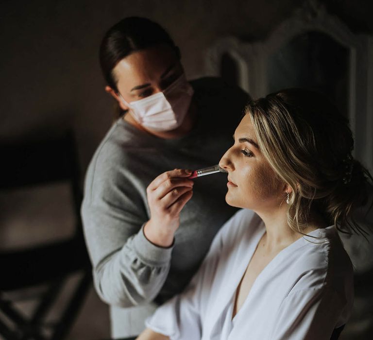 Bride in a white robe gets her makeup done for her wedding day 