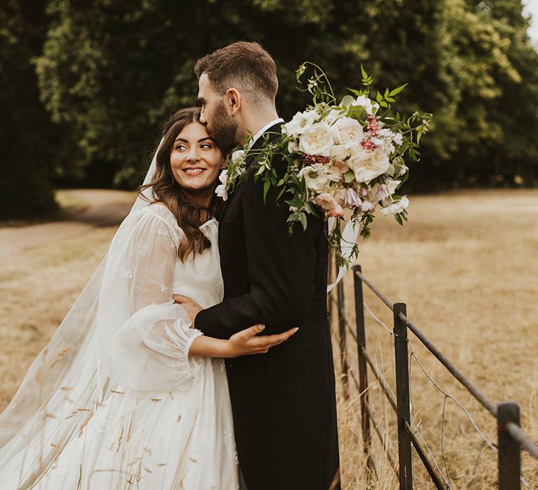 Groom in a morning suit kisses the bride on her forehead in a balloon sleeve wedding dress