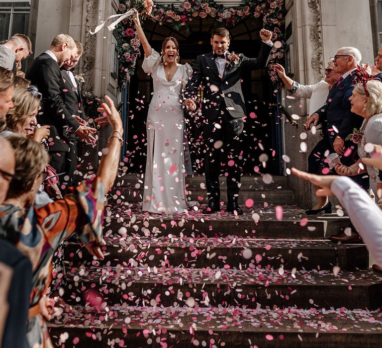 Bride in v neck wedding dress with puff sleeves and front slit and groom in black tux doing confetti walk at Somerset House wedding