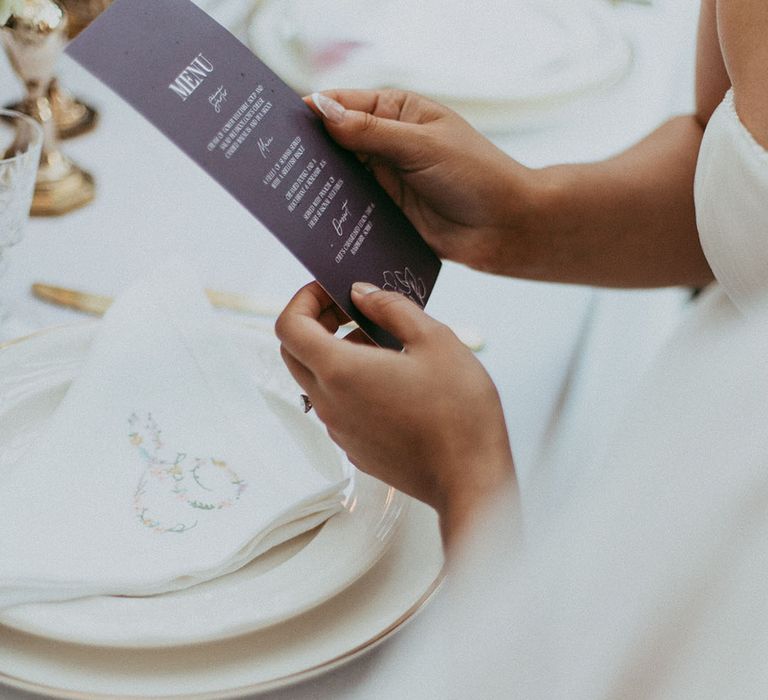 Bride reading lavender wedding menu at minimalistic wedding tablescape 