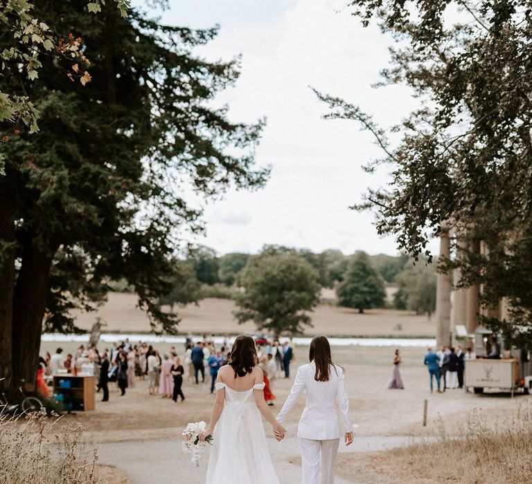 The brides walk hand in hand to their guests enjoying the summer weather outside at the Wilderness Reserve 